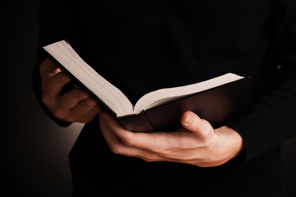 Hands holding open russian bible on black background - Foto, imagen