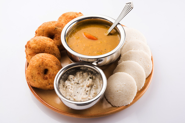Sambar vada & idli mit Sambar, Kokos-Chutney und rotem Tomaten-Chutney, indisches Gericht serviert in irdenem Teller und Schüssel über weißem Hintergrund, Vorderansicht, isoliert auf weißem Hintergrund - Foto, Bild