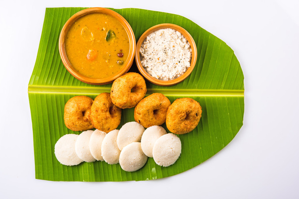 Sambar Vada & Idli with sambar, coconut chutney and red tomato chutney in earthen pots, served over green banana leaf over white background - Photo, Image