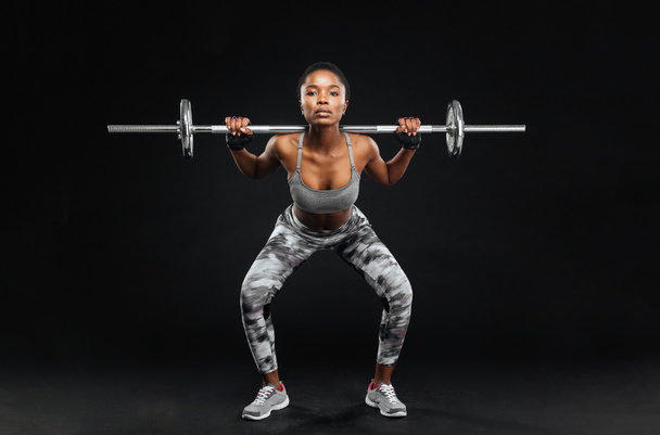 Close-up portrait of fitness girl doing squats with barbell - 写真・画像