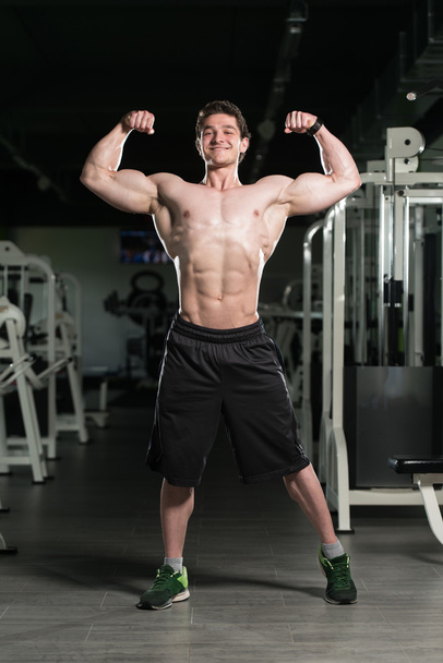 Bodybuilder Flexing Front Double Biceps Pose In Gym - 写真・画像