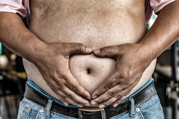 De gevaren van buik vet., zwaarlijvige Man in Jeans Squeeze het buik vet., zwaarlijvige Man is meer kans om te verstoppen slagaders en diabetes. - Foto, afbeelding