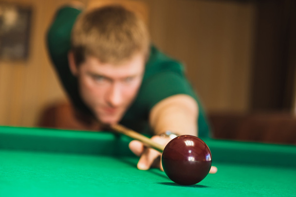 Details of the game of billiards. Red ball in the center of the frame. Player aiming cue in a billiard ball. Blurred person in the background. - Photo, Image