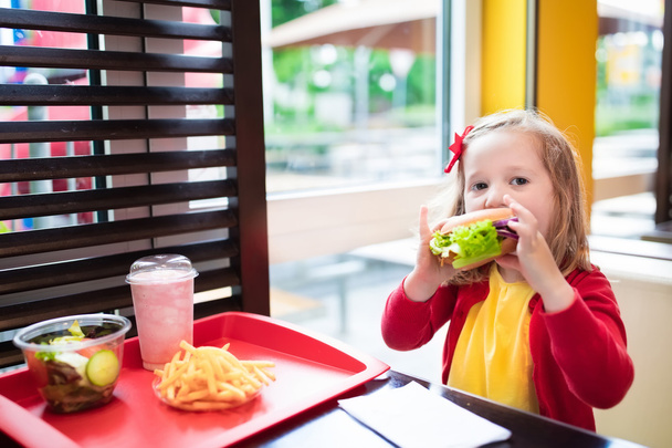 Bambina che mangia un hamburger nel ristorante fast food
 - Foto, immagini