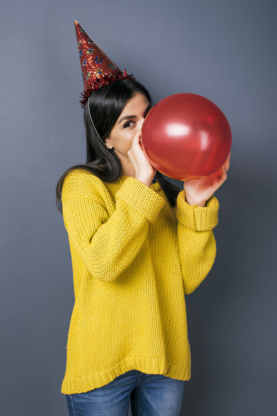 Girl in festive hat and yellow sweater blowing balloon - Φωτογραφία, εικόνα