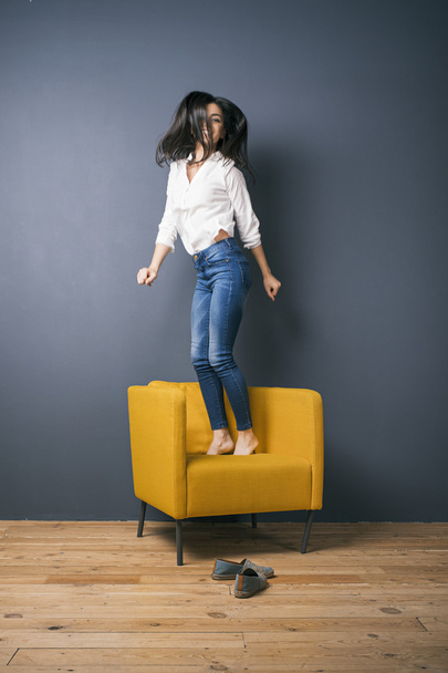 Armenian cheerful girl jumping on arm-chair - 写真・画像