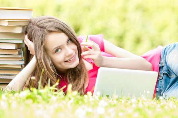 ラップトップ コンピューターを持つ草に横たわっている幸せな学生の女の子 - 写真・画像