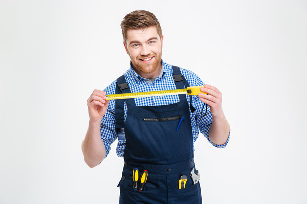 Cheerful young worker in overall smiling and holding measuring tape - Foto, afbeelding