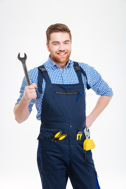 Cheerful attractive young worker in overall holding wrench - Foto, afbeelding