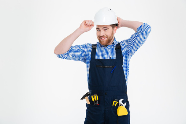 Portrait of happy bearded young builder in overall and helmet - 写真・画像