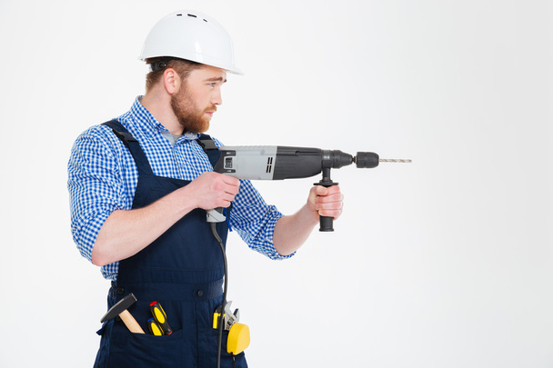 Profile of concentrated handsome young builder using modern drill - Foto, imagen