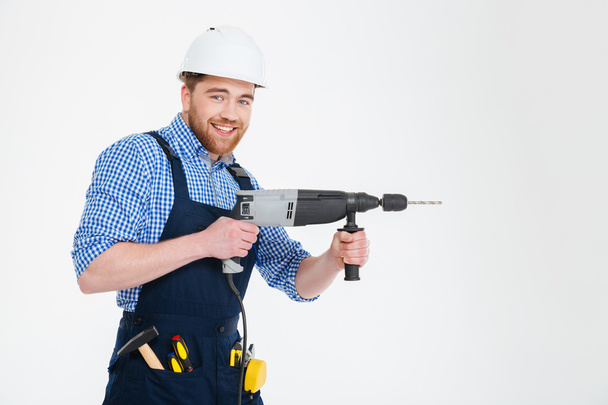 Happy attractive young builder smiling and using modern drill - Foto, Imagen