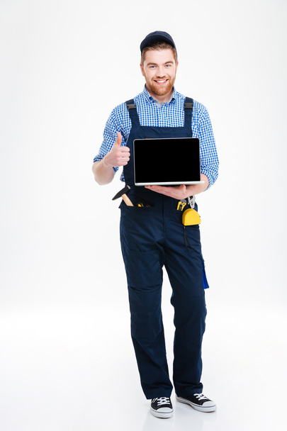 Man builder holding blank screen laptop and showing thumbs up - Fotoğraf, Görsel