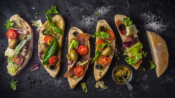 Slices of ciabatta with olives , tomatoes and basil on the black stone table wide screen - Fotoğraf, Görsel