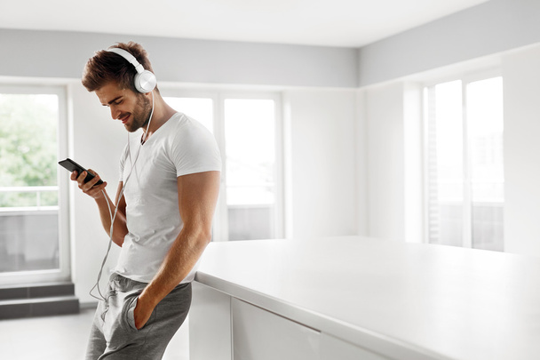 Man Listening To Music In Headphones Using Mobile Phone Indoors - Valokuva, kuva