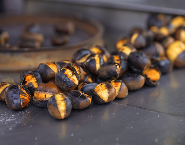 Macro roasted chestnuts with salt om metal surface. - Photo, Image