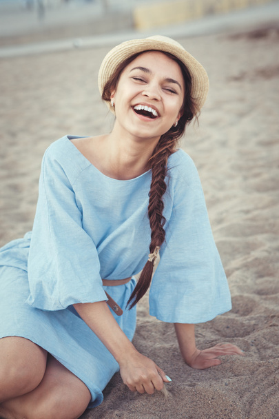 Muotokuva hymyilevä nauraa valkoinen valkoihoinen ruskeaverikkö nainen ruskettunut iho sininen mekko ja olki hattu istuu hiekkarannalla, auringonlasku kesäpäivänä, elämäntapa käsite
 - Valokuva, kuva