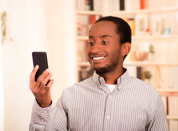 Handsome man wearing casual clothes holding up mobile phone looking at screen and smiling - Фото, зображення