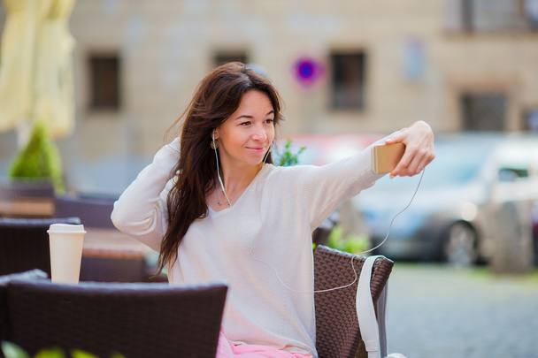 Joven mujer caucásica enviando mensaje y tomando autorretrato en café al aire libre
 - Foto, Imagen