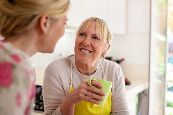 Mother and daughter talking, drinking coffee in kitchen - Photo, image
