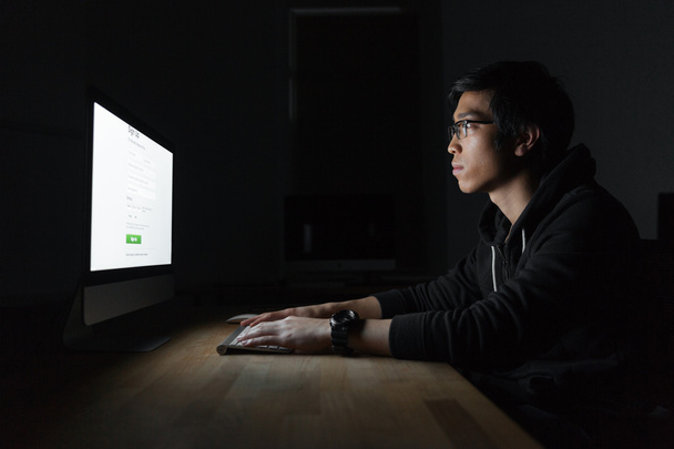 Ασιατικές Oμορφος νέος χρησιμοποιώντας υπολογιστή σε σκοτεινό δωμάτιο - Φωτογραφία, εικόνα