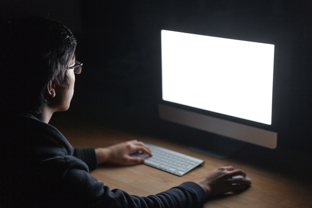 Man sitting at table and using computer in dark room - Φωτογραφία, εικόνα