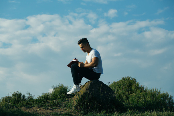 Pensive muscular man with book outdoor - Foto, afbeelding
