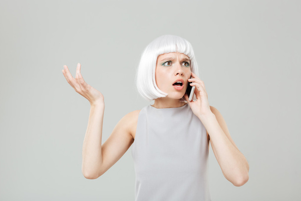 Puzzled worried woman in blonde wig talking on mobile phone - 写真・画像