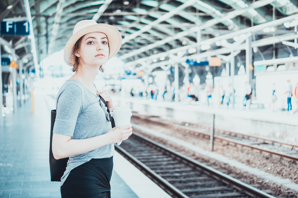 Rustige vrouw in hoed wachten onder trein station dak - Foto, afbeelding