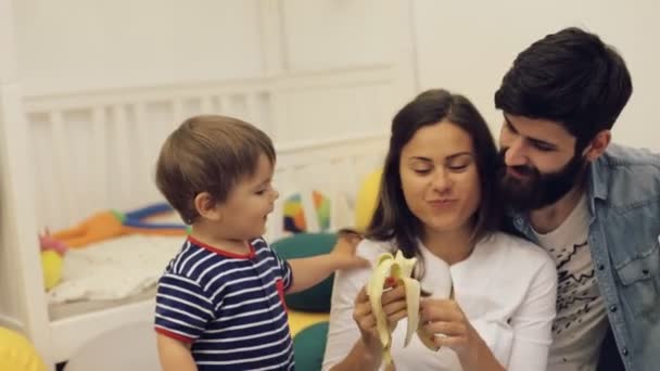 Onnelliset vanhemmat ruokinta lapsi poika terveellistä ruokaa kotona, söpö vauva syö banaania sisätiloissa
 - Materiaali, video