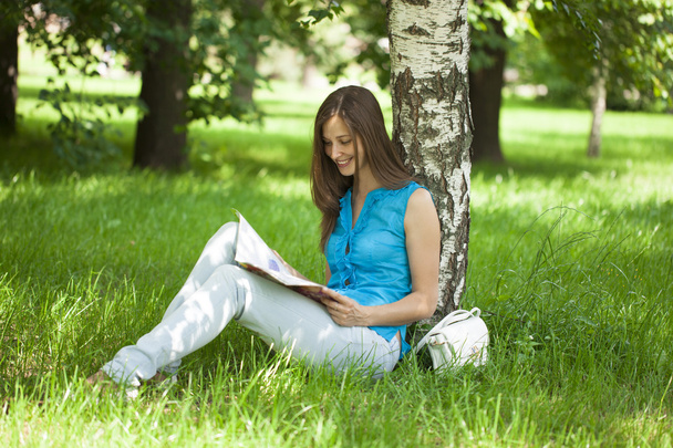 Happy woman leafing through a magazine while sitting in the summ - Фото, изображение