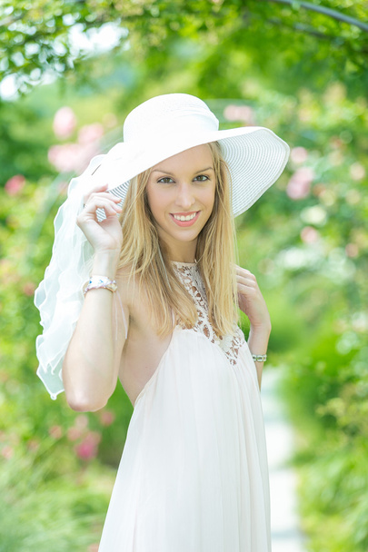 Portrait of beautiful natural young woman with white hat in the rose garden - Fotoğraf, Görsel