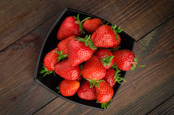 Strawberries in black plate. wooden background top view - Fotó, kép