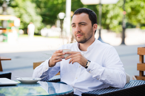 Уверенный в себе успешный бизнесмен в костюме наслаждаясь чашкой кофе во время обеденного перерыва на работе в современном ресторане, молодой умный человек или предприниматель расслабляется в открытом кафе глядя задумчиво
 - Фото, изображение