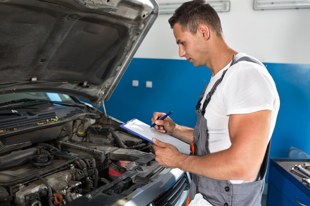 Mechanic man holding clipboard and check the car - Foto, Imagen