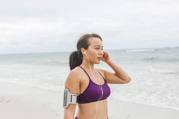 Läuferin bereitet sich auf Outdoor-Training am Strand vor und setzt Kopfhörer auf - Foto, Bild