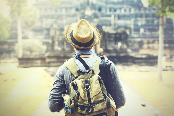Young traveler wearing a hat with backpack and tripod - at Angkor Wat, Siem Reap, Cambodia - Фото, изображение