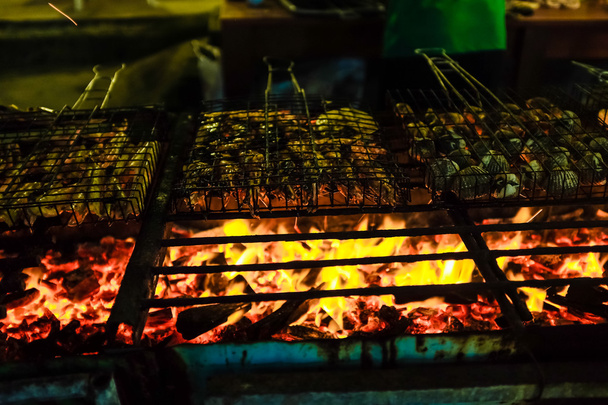 Ряд вкусные креветки рыба и скорлупа на гриле с пламенем в фоновом режиме ночью
 - Фото, изображение