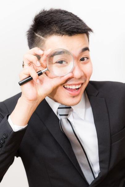 Geschäft asiatische Mann Blick auf Kamera durch Lupe Nahaufnahme auf weiß - Foto, Bild