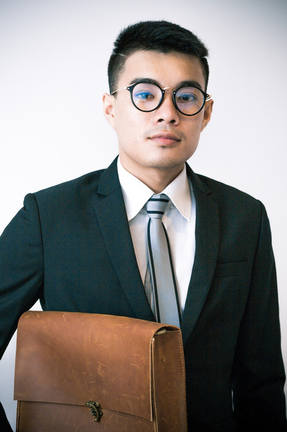 Aziatische glimlachend jonge business man bril een handgemaakte lederen draagtas op witte achtergrond - Foto, afbeelding