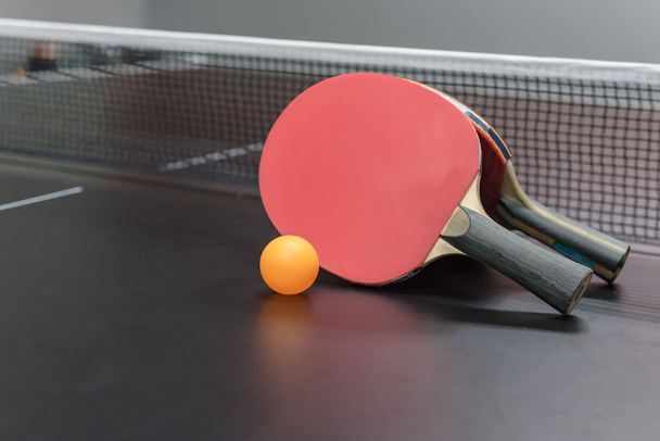 oranžová koule s červeným stolní tenis rakety na černém stole - Fotografie, Obrázek