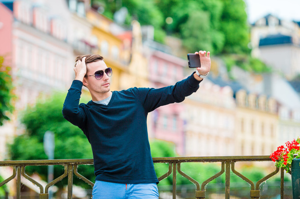 Турист фотографирует путешествия со смартфоном во время летних каникул. Молодой привлекательный турист делает селфи фото с мобильного телефона на открытом воздухе наслаждаясь праздников туристических назначения в туризме и
 - Фото, изображение