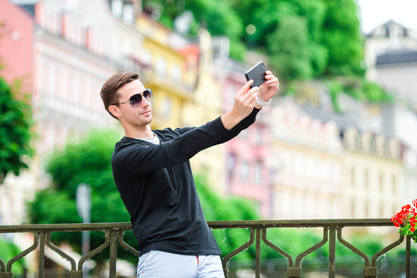 Tourist man taking travel photos with smartphone on summer holidays. Young attractive tourist taking selfie photo with mobile phone outdoors enjoying holidays travel destination in tourism. - Foto, immagini