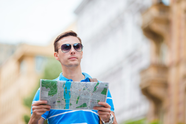 Άνθρωπος τουρίστρια με χάρτη της πόλης και σακίδιο στην Ευρώπη. Καυκάσιος αγόρι κοιτάζοντας το χάρτη της Ευρωπαϊκής πόλης σε αναζήτηση αξιοθέατων. - Φωτογραφία, εικόνα