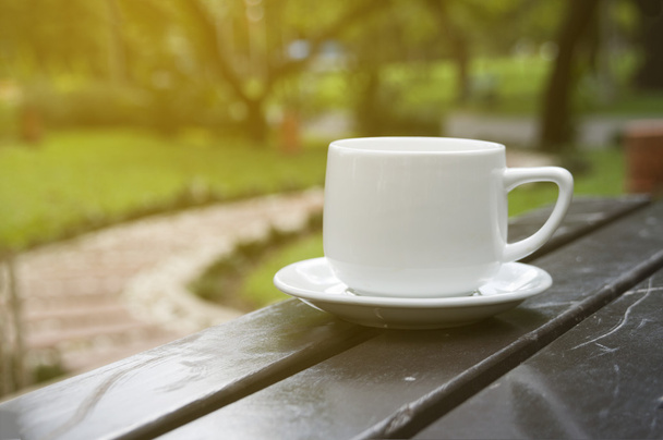 kuppi kahvia pöydällä puutarhassa aurinkoisena päivänä, hämärtynyt
 - Valokuva, kuva