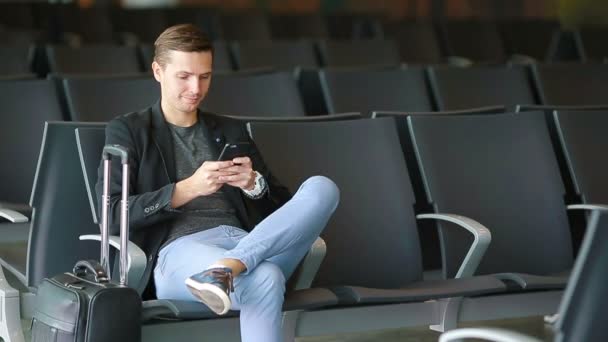 Městské obchodní muž mluví o chytrý telefon cestování uvnitř na letišti. Neformální mladý podnikatel nosit sako. Pohledný muž modelu. Mladý muž se mobil při čekání na letišti - Záběry, video