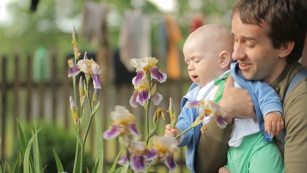 Η μητέρα αγγίζει το μωρό με ένα λουλούδι μετά από μια βροχή. Όμορφο αγόρι λιγότερο από ένα χρόνο - Πλάνα, βίντεο