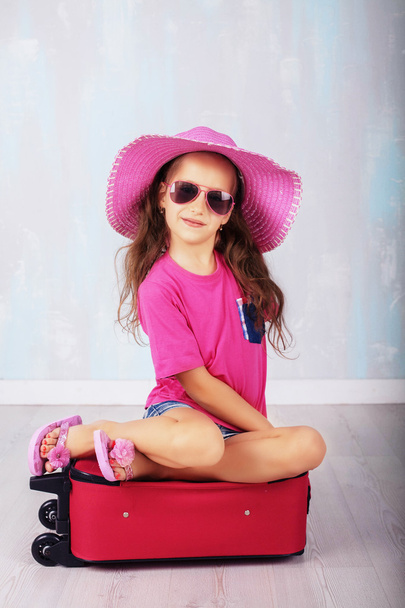 child with long hair in pink sitting on a suitcase - Fotografie, Obrázek