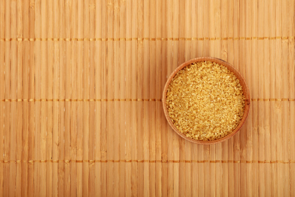 Wooden bowl of brown cane sugar on bamboo mat - Photo, Image