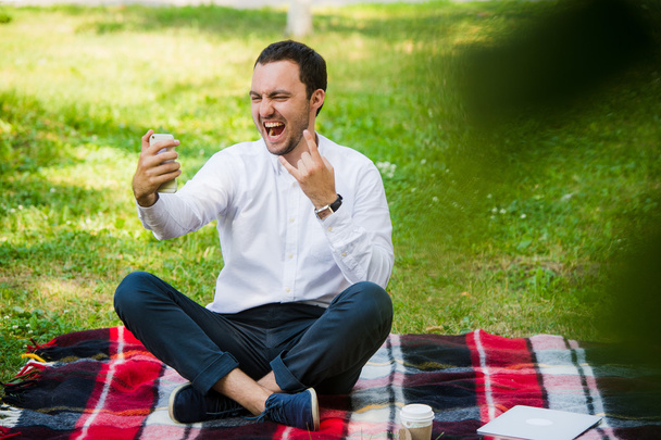Photo of handsome nice guy outdoors at morning. Young man smiling and making selfie photo on mobile phone with cool expressions - Foto, Imagem